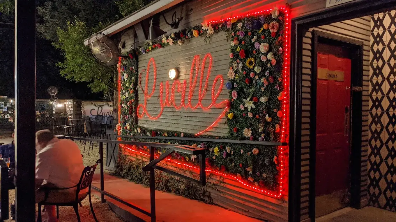 Lucille's red neon script sign framed by a wall of flowers on the patio at night