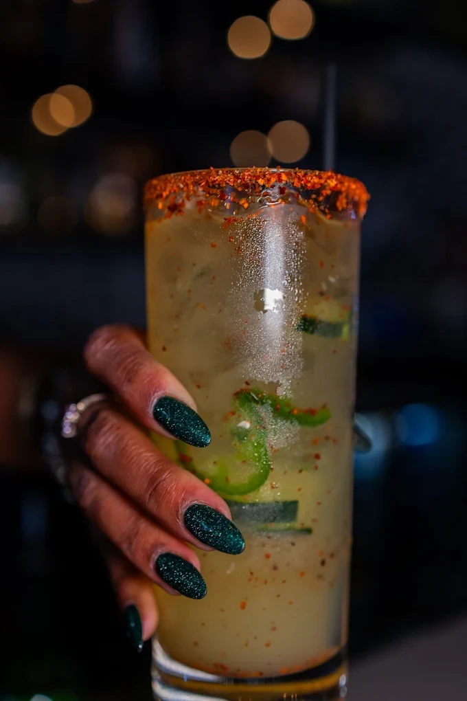 A spicy El Jefe Loco margarita with jalapeño, cucumber and a chili salt rim, held up at the bar