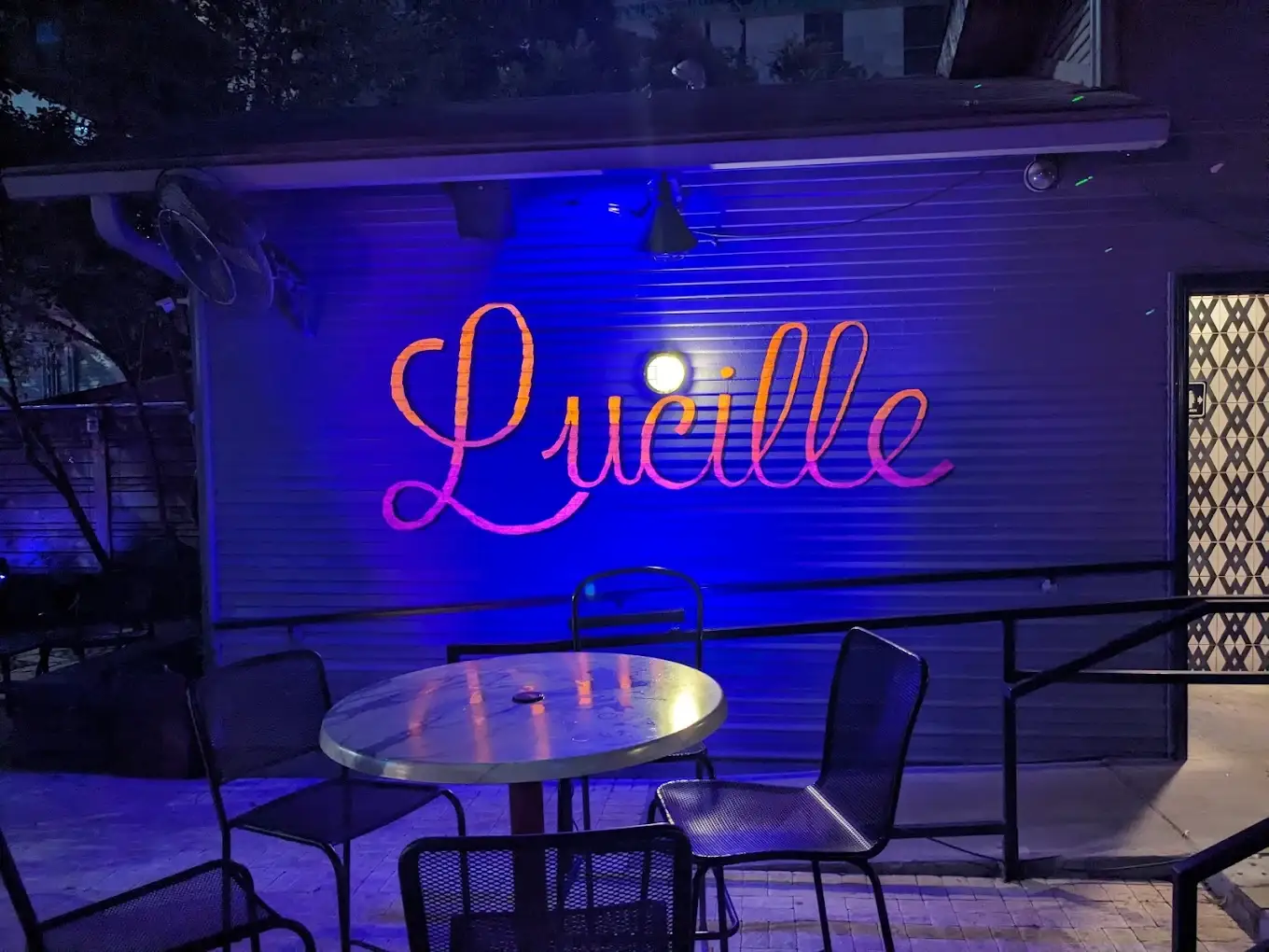 Lucille script sign glowing pink and orange against a blue-lit wall