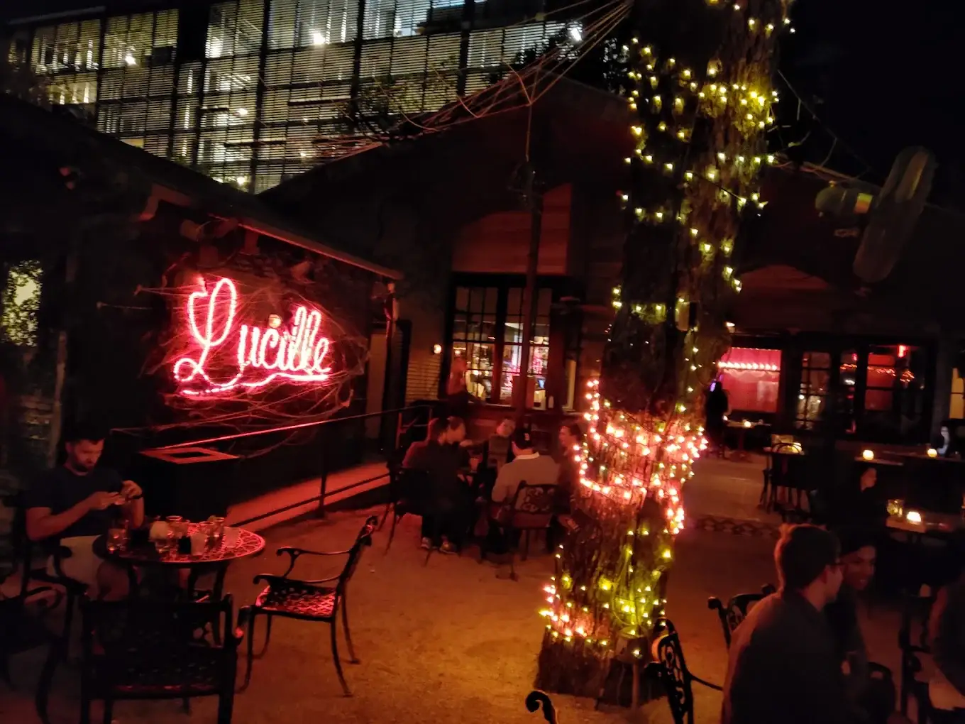 Neon Lucille sign and a tree wrapped in string lights over the patio at night
